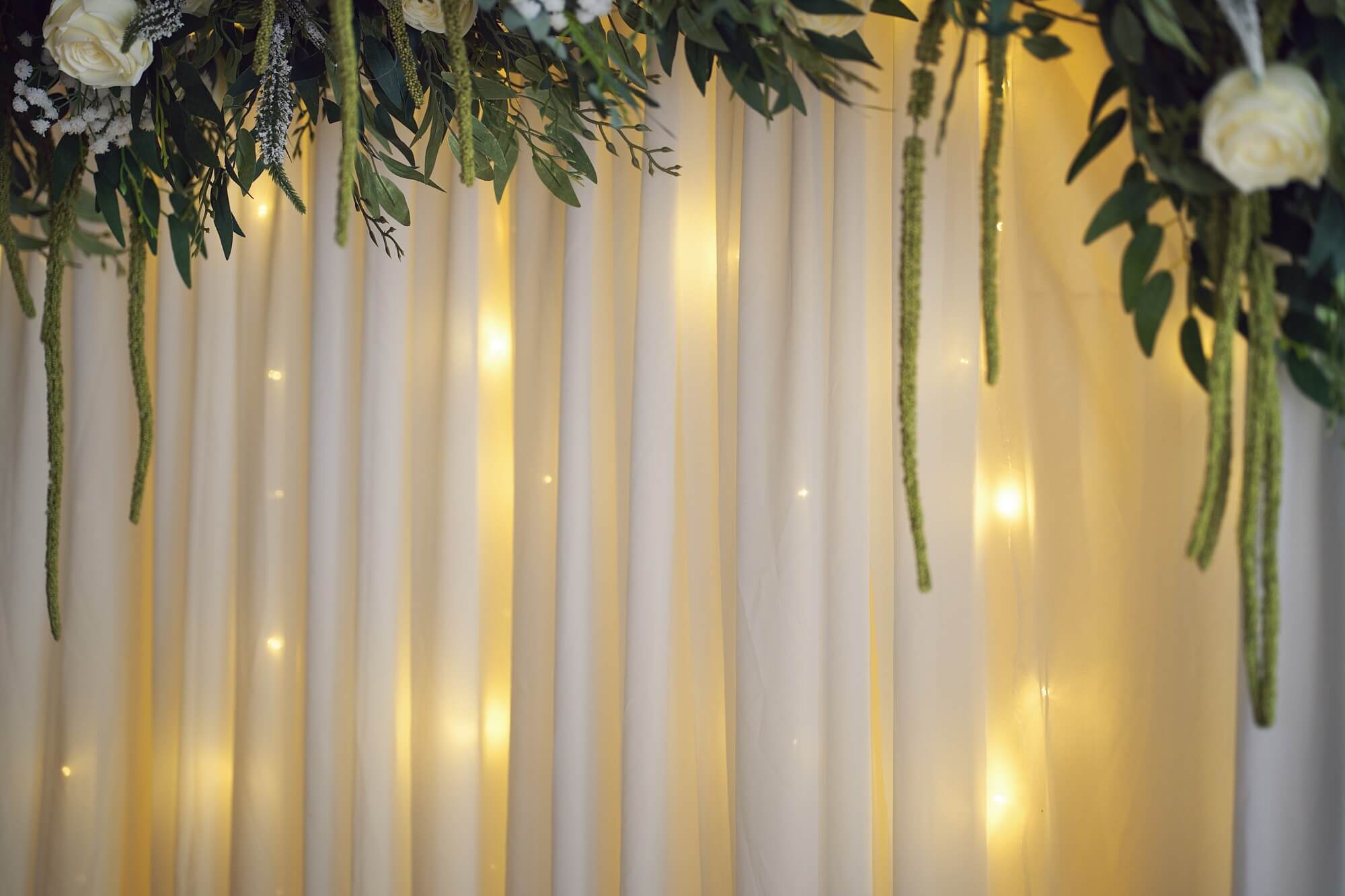 White draped wedding backdrop with soft lighting and floral accents