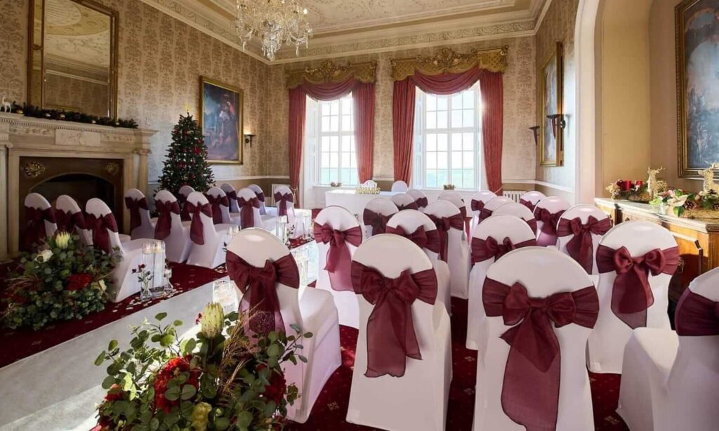 Elegant venue styling with burgundy chair sashes, floral arrangements and a classic wedding ceremony setup.