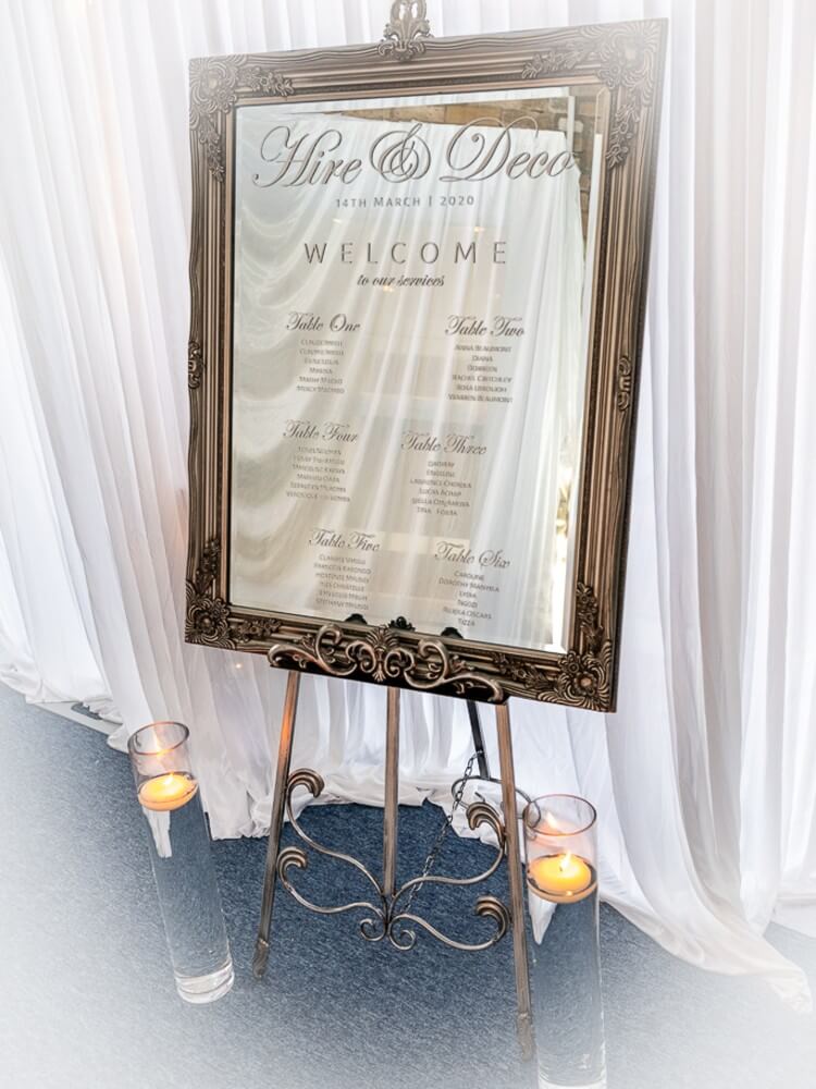Elegant mirror welcome sign with candles, showing what room dressing includes for a beautifully styled event.