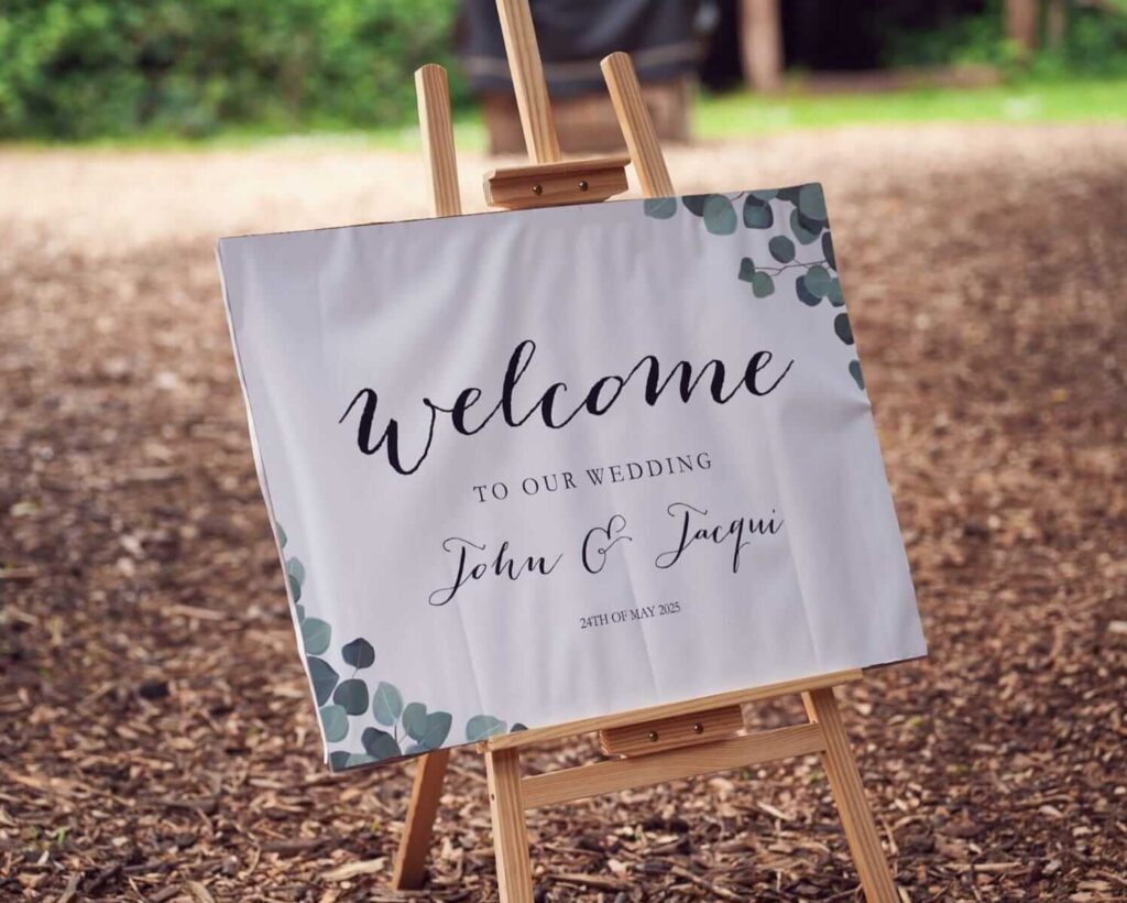 Room dressing with wedding welcome sign on wooden easel at outdoor entrance.