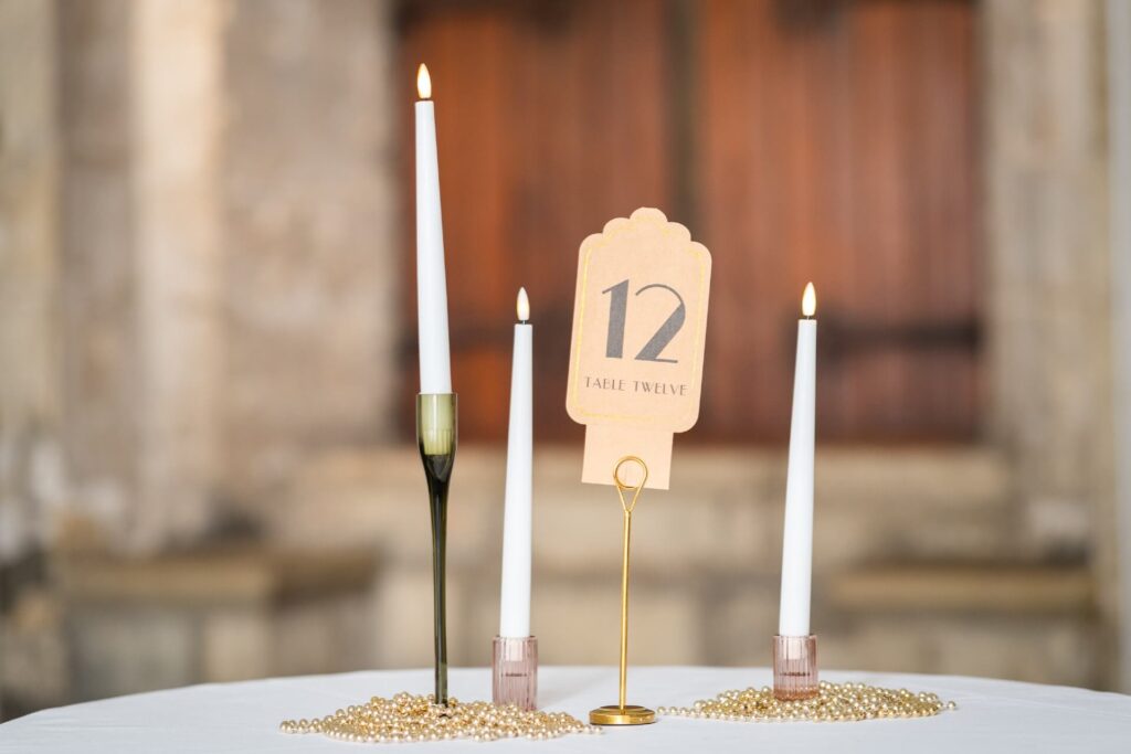 DIY wedding hire number for a table with taper candles and gold beads on a white table.