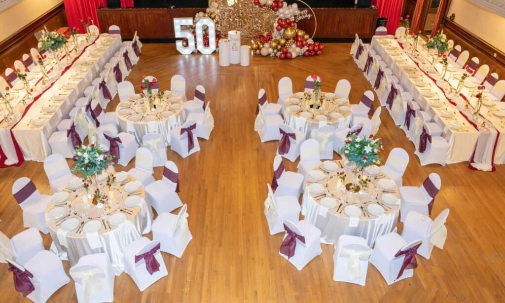 Aerial view of 50th birthday banquet styled by an event planner with round and long tables, white chair covers and burgundy sashes.