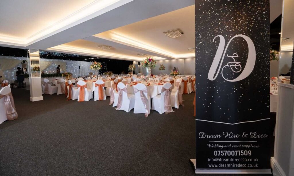 Wedding reception room styled by event planners with round tables, white chair covers and peach sashes.