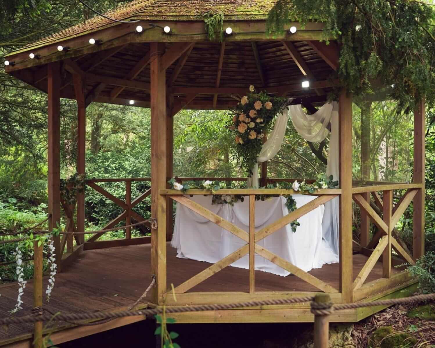 Forest wedding gazebo decorated with drapes and flowers for an outdoor ceremony.