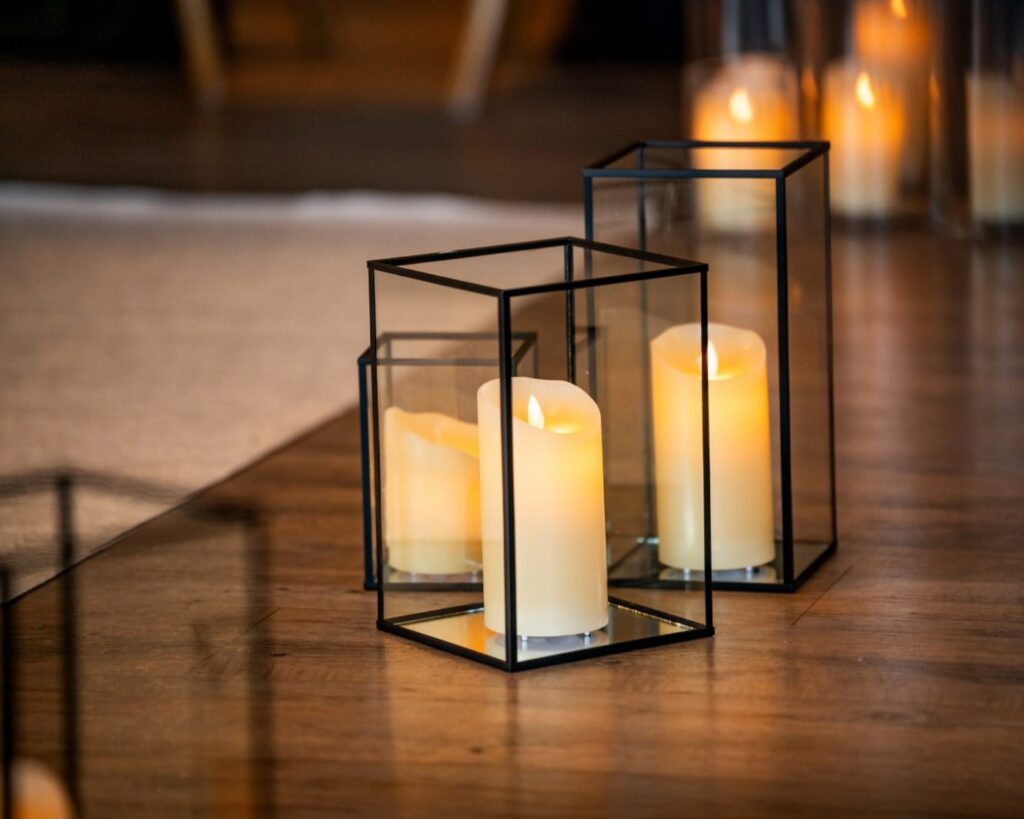 Rustic wedding lighting with black frame glass lanterns and warm candles on a wooden floor.