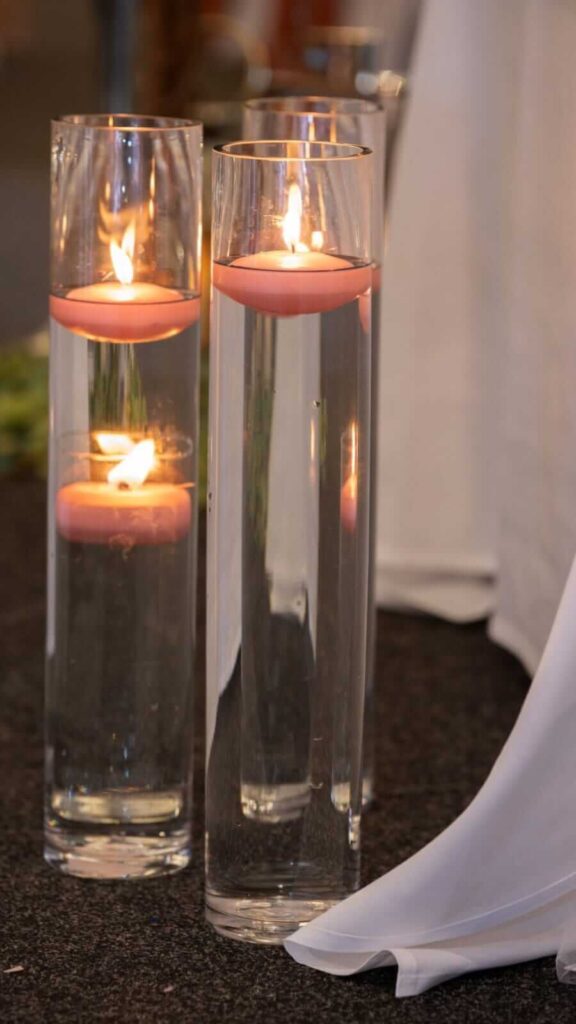 Tall glass vases with pink floating candles creating soft event lighting.