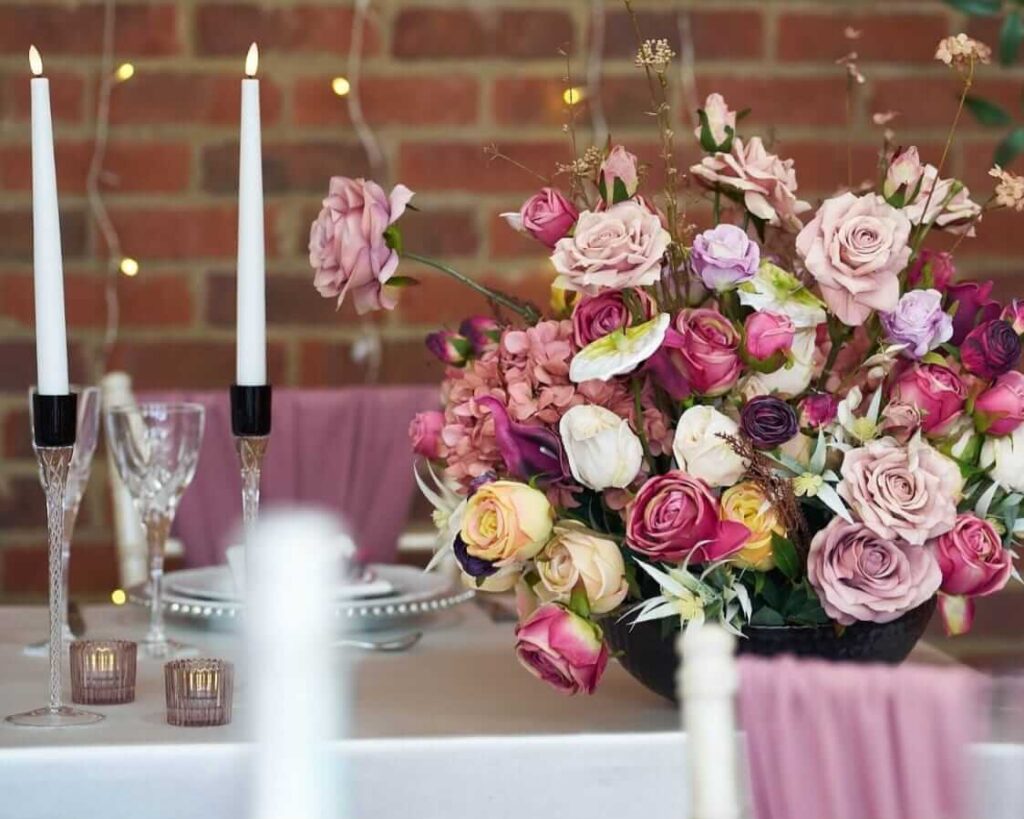 Romantic table centrepiece with roses and candles under cool white lighting.