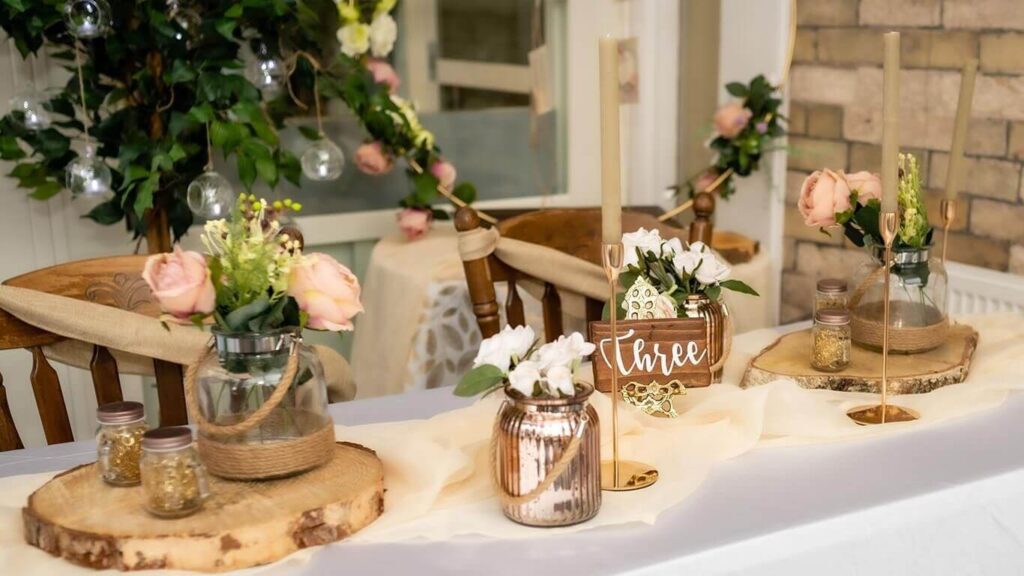 Rustic wedding top table decorated with wood slices, bud vases of roses and soft candlelight.