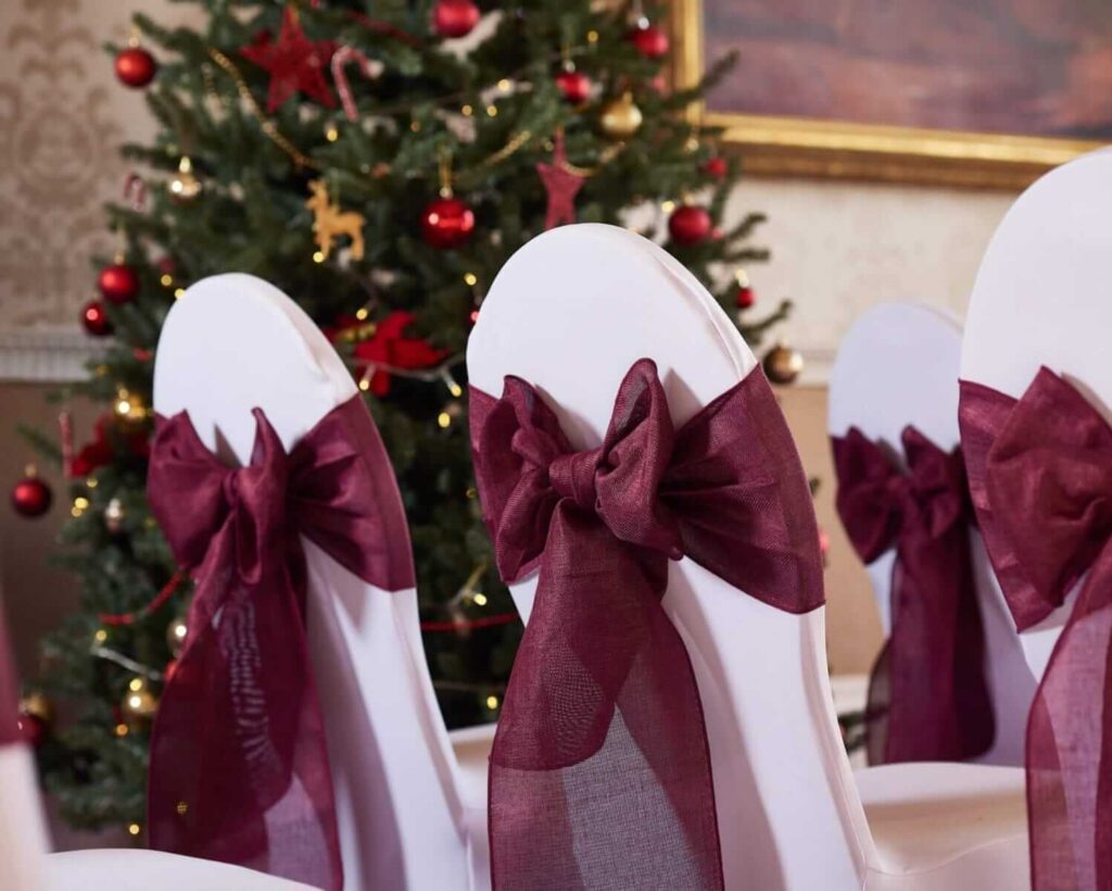 Burgundy organza sash bows on covered chairs for festive colour matching