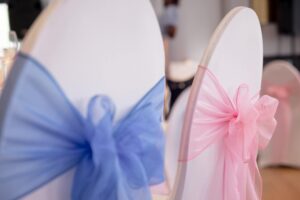 Covered chairs with pink and blue chiffon sash bows at an event setup