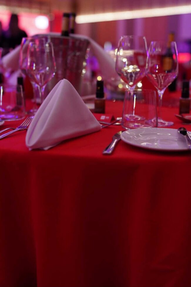 Red table cloth on a round event table with white napkin place setting