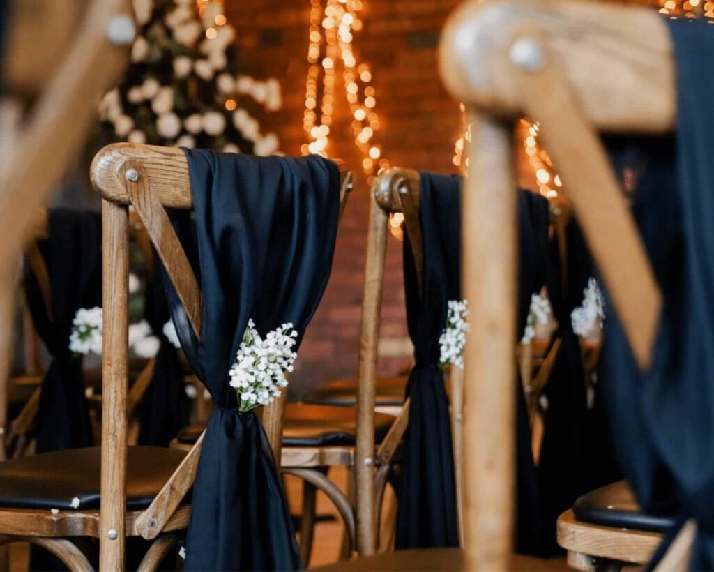 Chair back decorations with black drapes and white florals on cross-back chairs