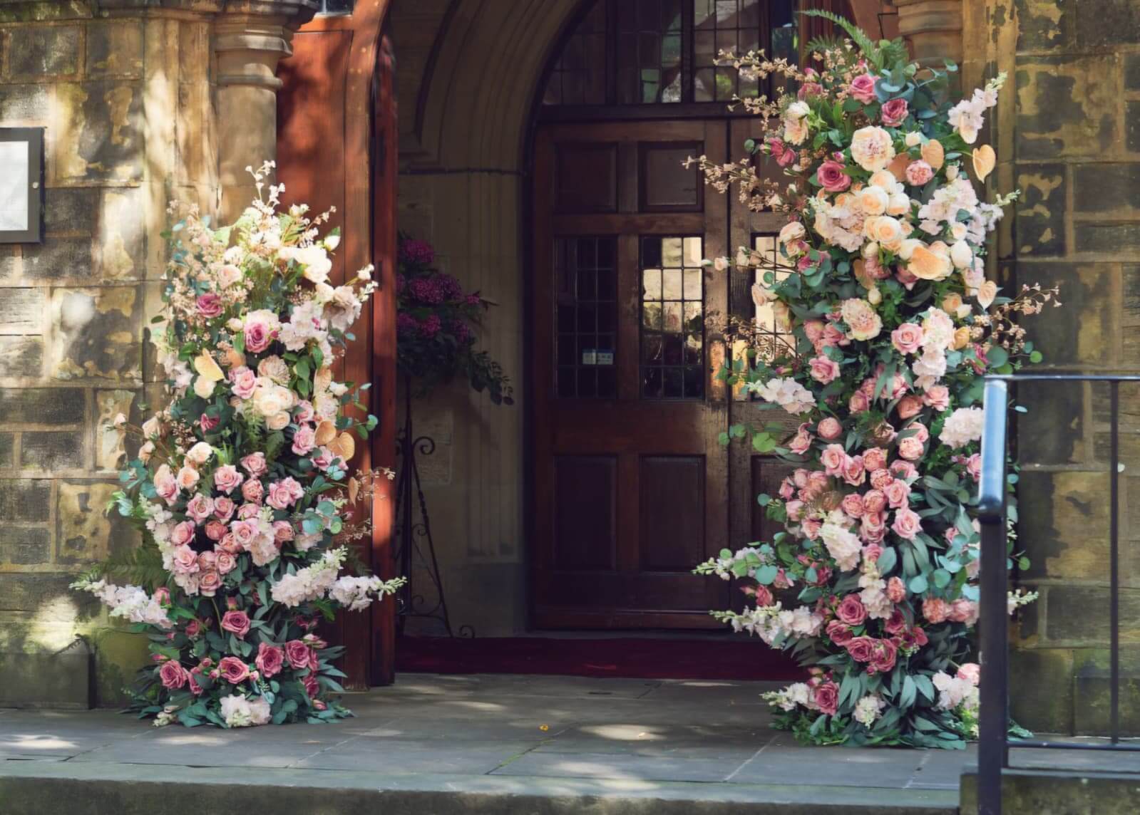 Broken floral arch hire with two pink and white flower pillars framing a wedding venue entrance