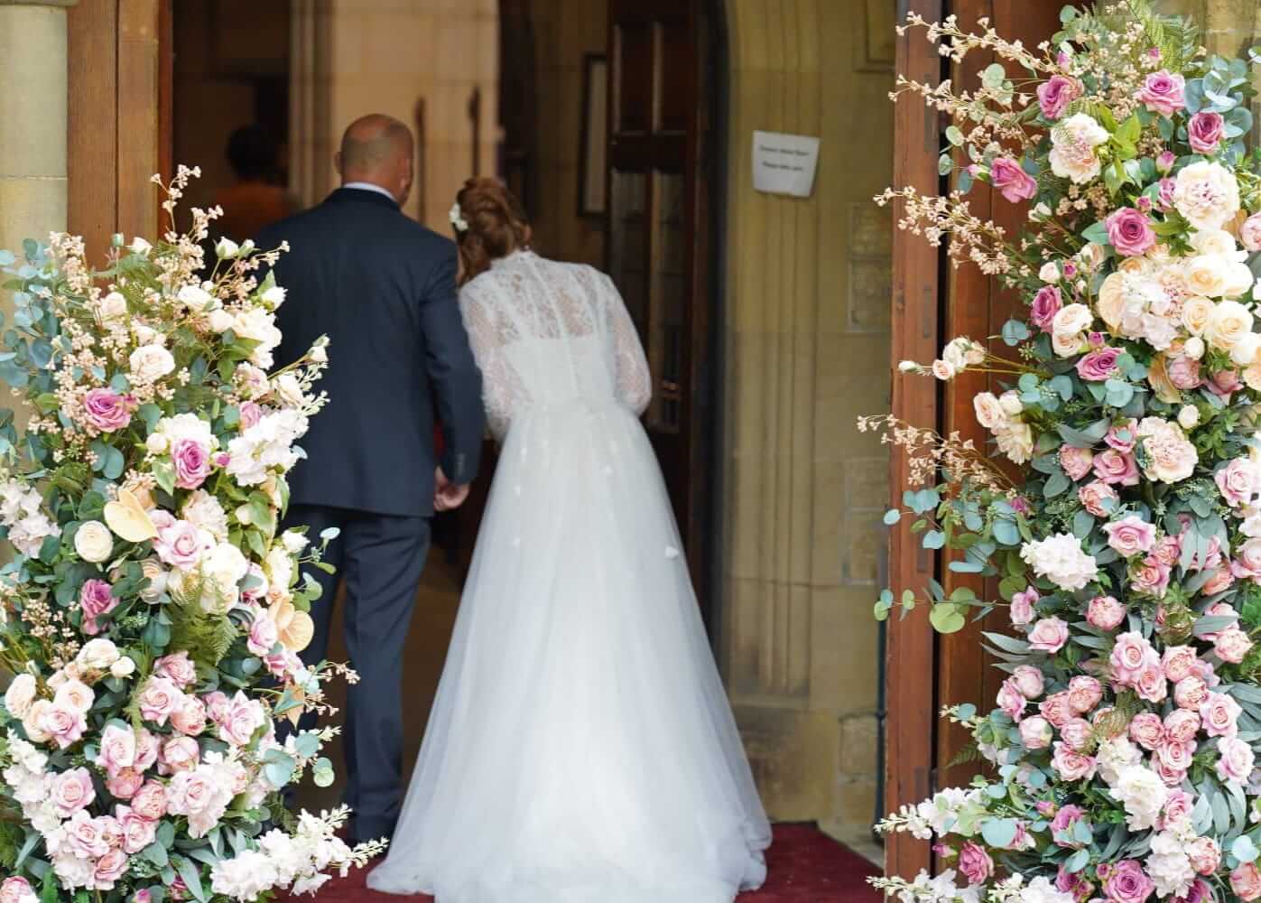 Bride entering between two pink and white pillars forming a broken wedding arch