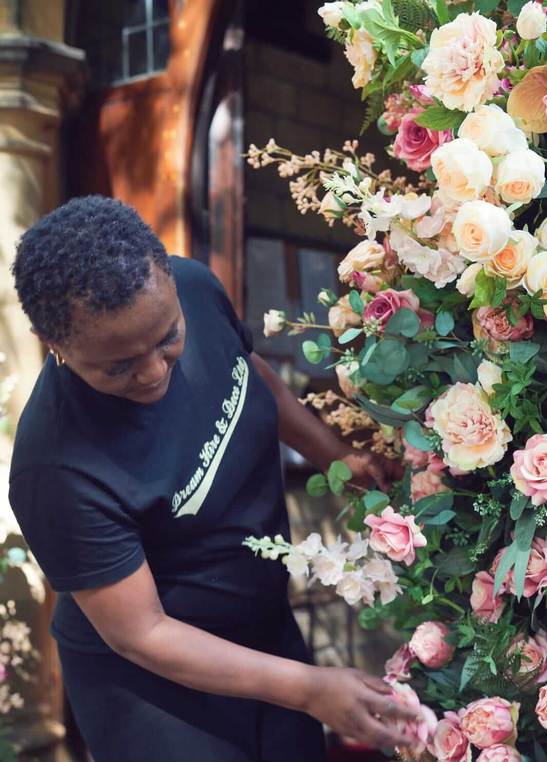 Dream Hire & Deco stylist arranging pink flowers on a floral pillar arch