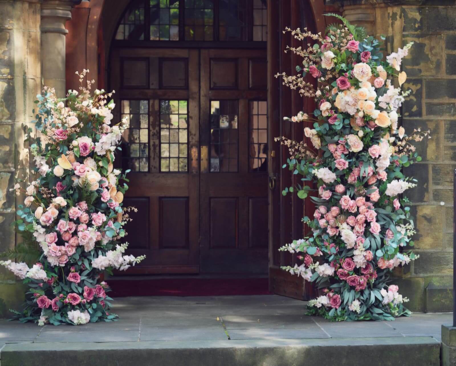 Broken floral arch hire with two staggered pink and white pillars framing a venue doorway